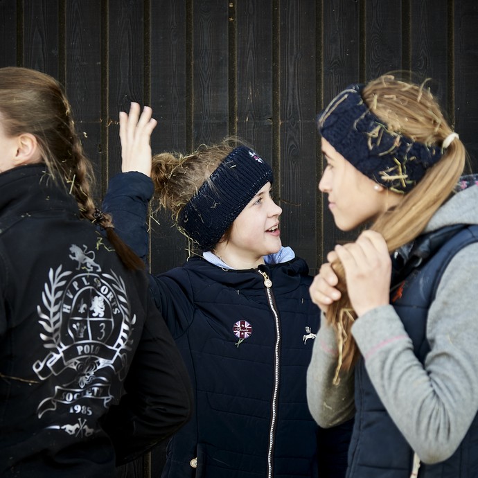 Vier Mädchen stehen vor einer dunklen Holzwand und lächeln. Sie alle haben Stroh in ihren Haaren. (vergrößerte Bildansicht wird geöffnet)