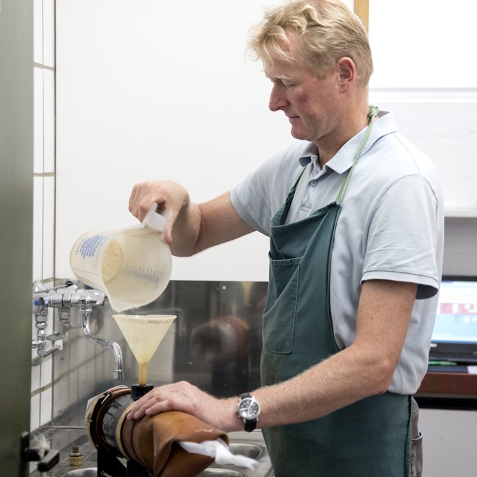 Ein blonder Mann mit grüner Schürze füllt Wasser durch einen Trichter in ein breites, kurzes Rohr. Dieses wird zur Absamung von Deckhengsten genutzt. (vergrößerte Bildansicht wird geöffnet)