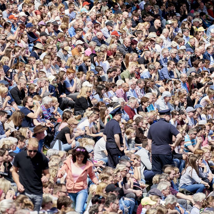 Eine große Anzahl von Menschen sitzt auf Zuschauertribünen. Der Blick der Menschen ist zur rechten Bildseite gewandt. (vergrößerte Bildansicht wird geöffnet)