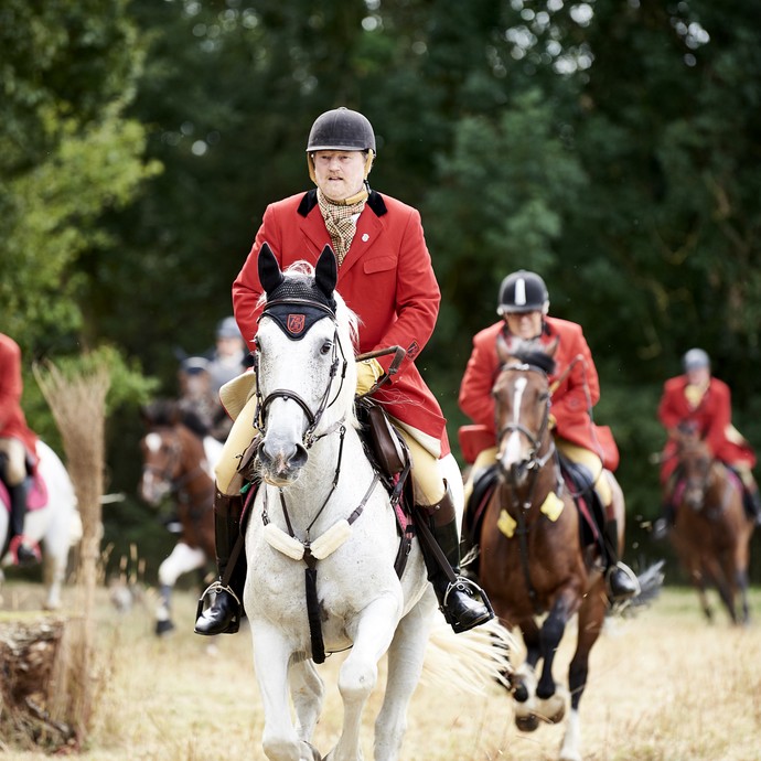 Traditionell in rot gekleidete Reiter einer Schleppjagd galoppieren über ein Feld auf die Kamera zu. (öffnet vergrößerte Bildansicht)