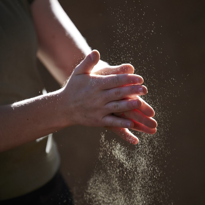 Jemand klopft Sand von seinen Händen. Die Sandkörner schimmern im Gegenlicht. (vergrößerte Bildansicht wird geöffnet)
