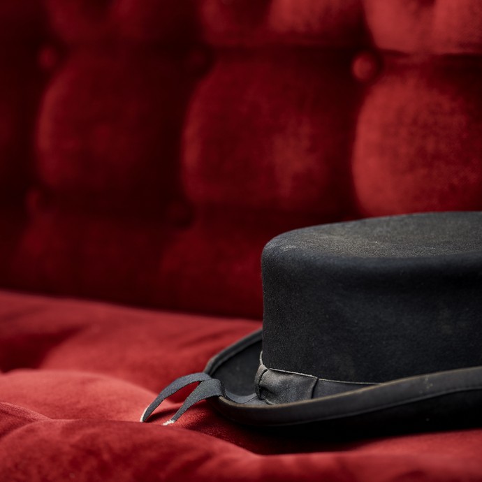Ein schwarzer Hut liegt auf einer mit rotem Samt gepolsterten Sitzbank. (öffnet vergrößerte Bildansicht)