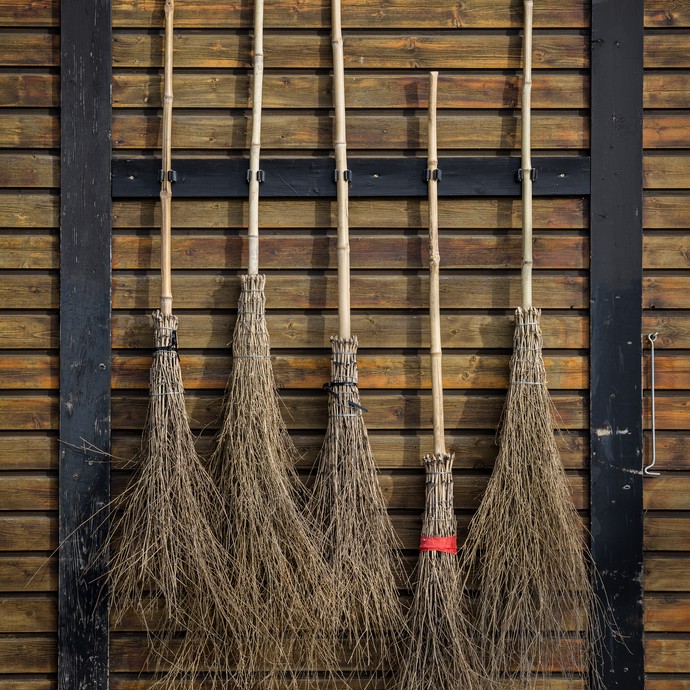 An einer Holzwand hängen fünf Reisigbesen. (öffnet vergrößerte Bildansicht)